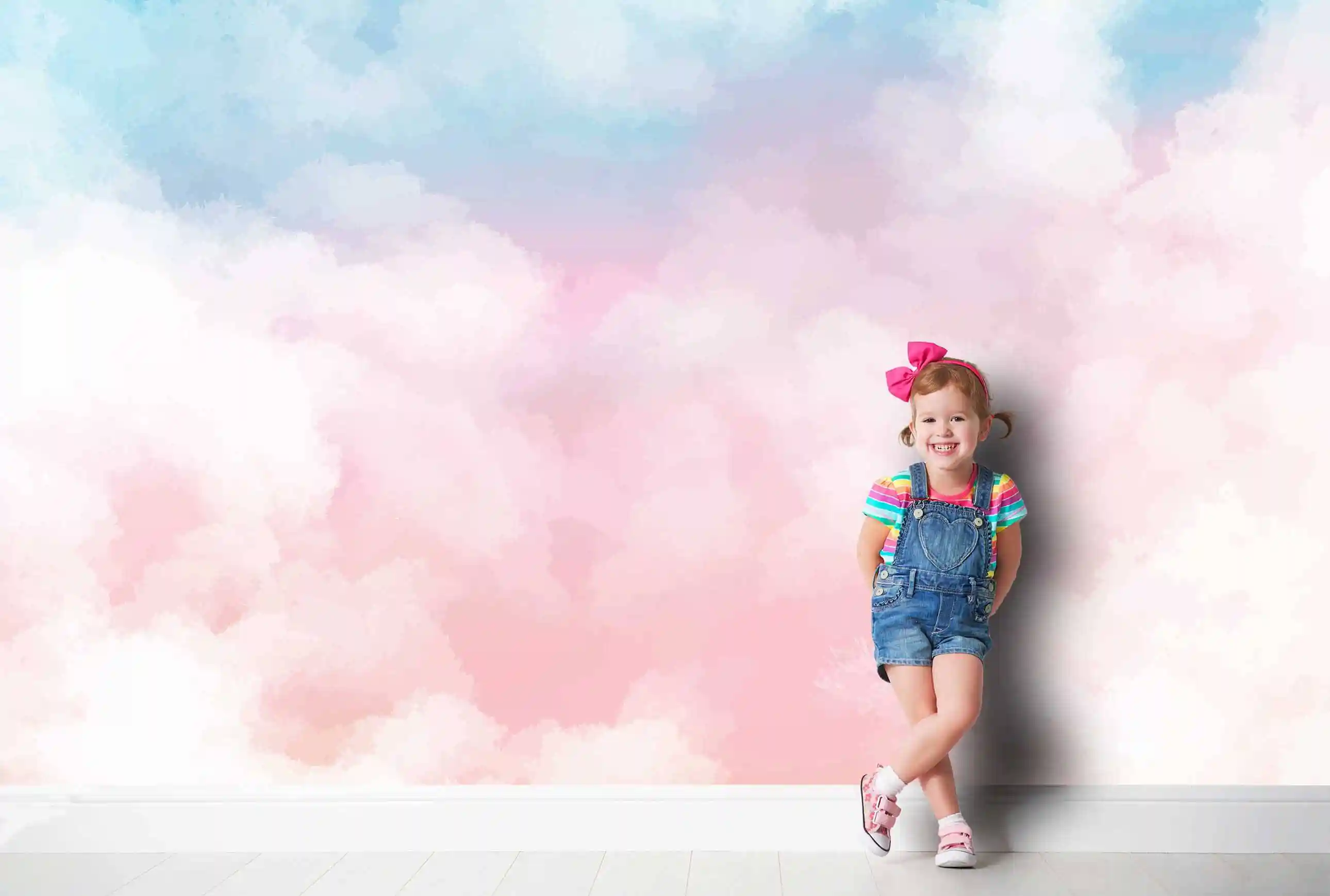 Pastell Wolken Tapete mit rosa-blauen Wolken, davor lehnt ein Mädchen mit rosa Schleife und Latzhose an der Wand